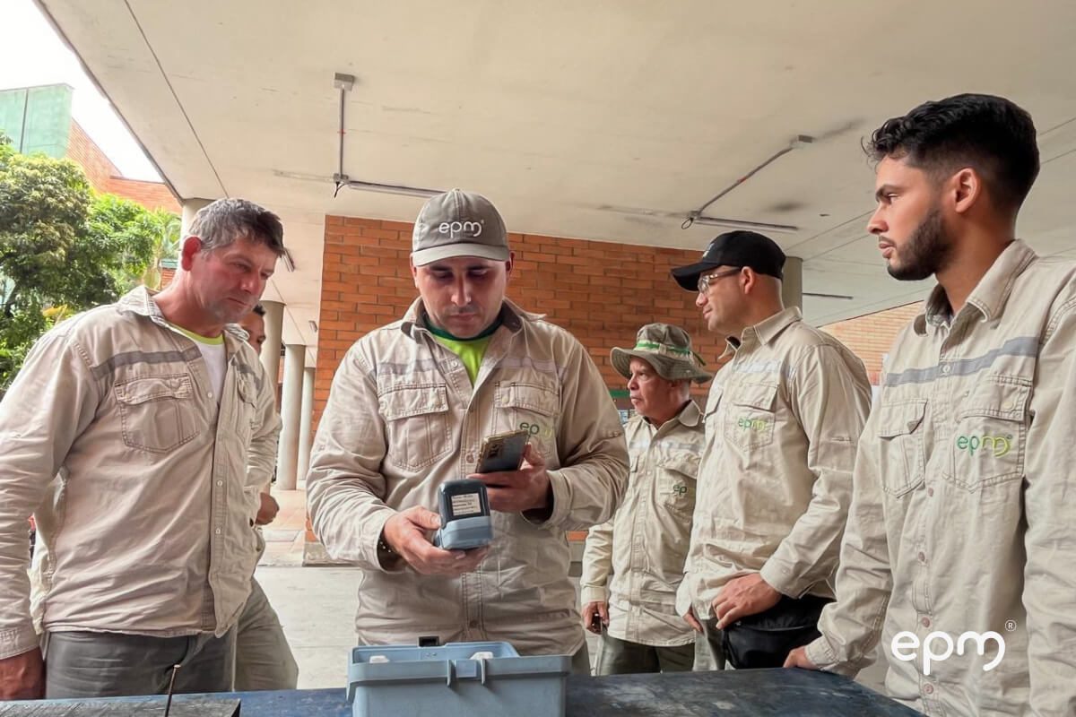 Fotografía de un grupo de trabajadores de EPM revisando dispositivos o documentos bajo techo, en un entorno operativo.
