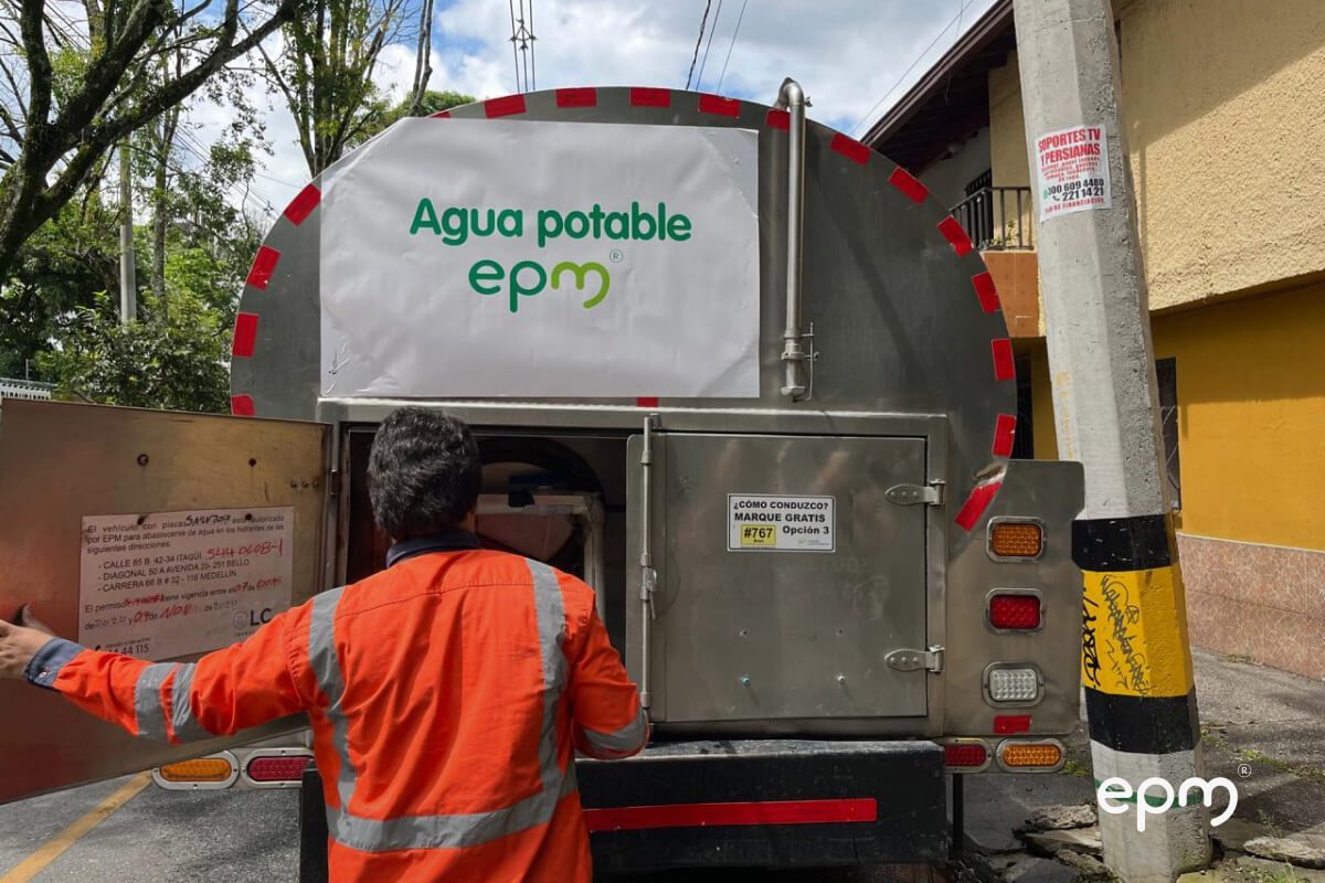 Fotografía de un trabajador con chaqueta naranja conectando una manguera a un camión cisterna de EPM rotulado con “Agua potable”