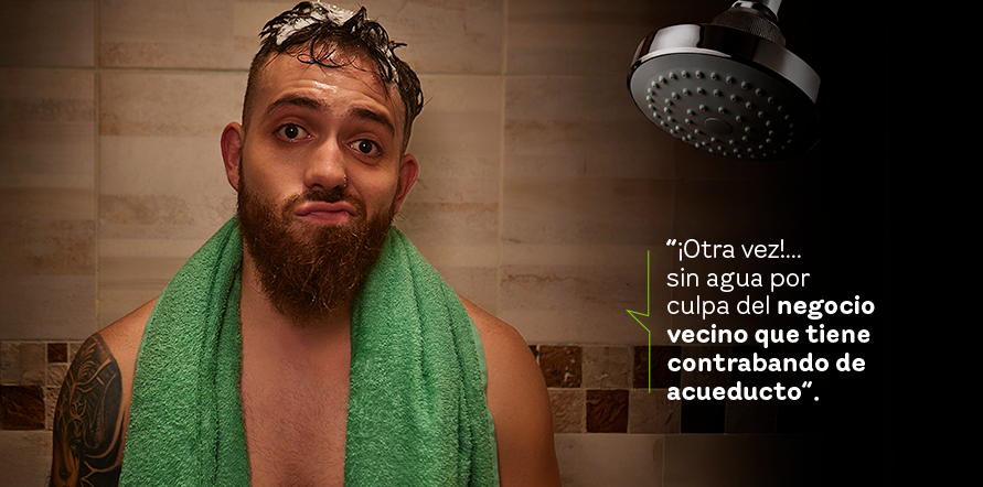 Hombre con el pelo mojado y toalla verde en el cuello en el baño donde se observa ducha y baldosa color café