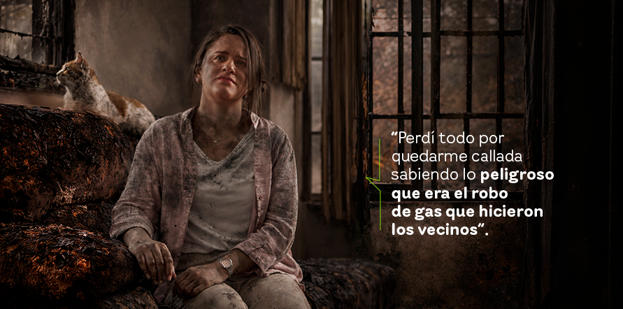 Mujer con ropa color blanca llena en una casa que ha sido incinerada por gas. Al fondo se observa un gato mirando por la ventana