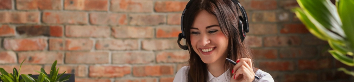 Mujer sonriente con auriculares y micrófono trabajando frente a una pared de ladrillo