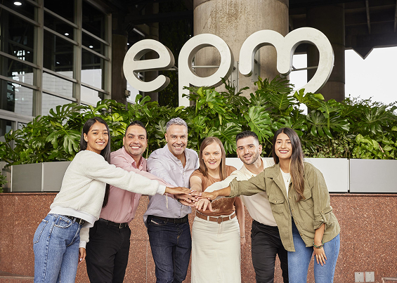 Equipo diverso de colaboradores de EPM posando juntos frente al logotipo corporativo