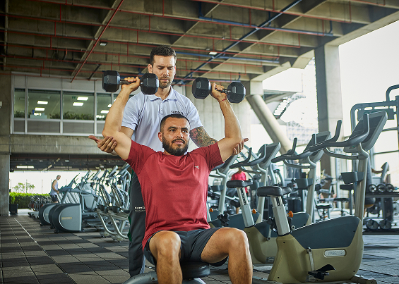 Instructor guía a un hombre mientras realiza ejercicio con pesas en el gimnasio corporativo