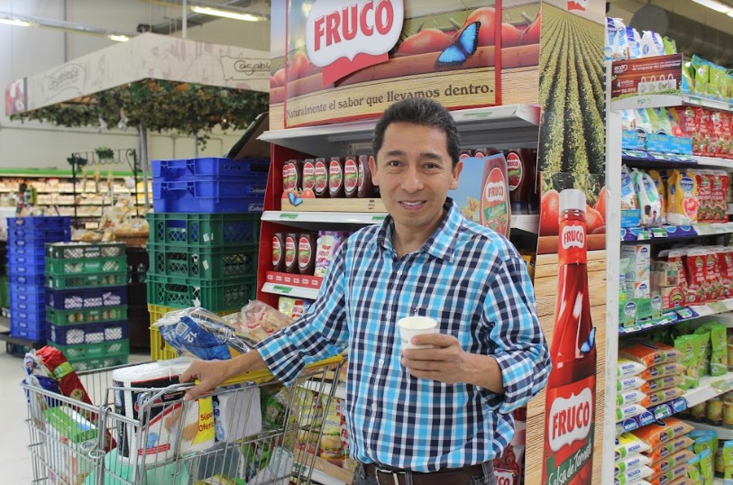 imágen de hombre con camisa a cuadros sonriente sosteniendo un producto en un supermercado.