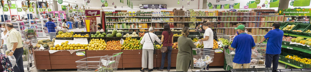 Personas comprando frutas y verduras en supermercado con estantes llenos de productos frescos