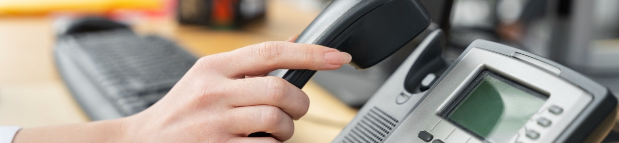 Primer plano de la mano de una persona descolgando el auricular de un teléfono digital sobre un escritorio de oficina