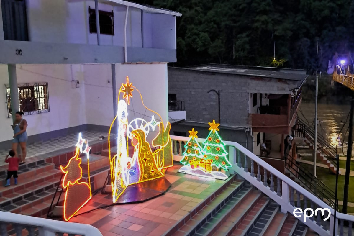 Figuras navideñas alumbrando sobre escalas de color café. Al fondo se observa casa de color blanco