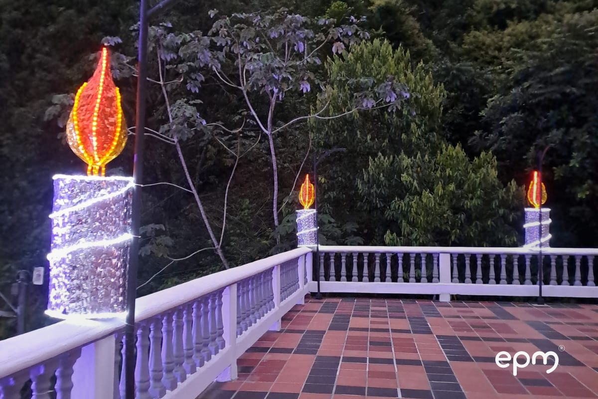 Figura en color rojo y amarillo sobre muro muro. Al fondo se observan árboles