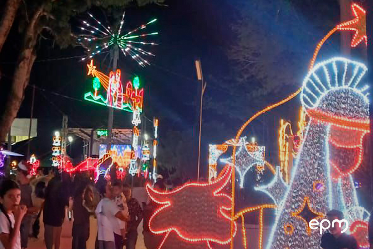 Personas reunidas observando alumbrado navideño de EPM. Al fondo se observan figuras navideñas alumbrando