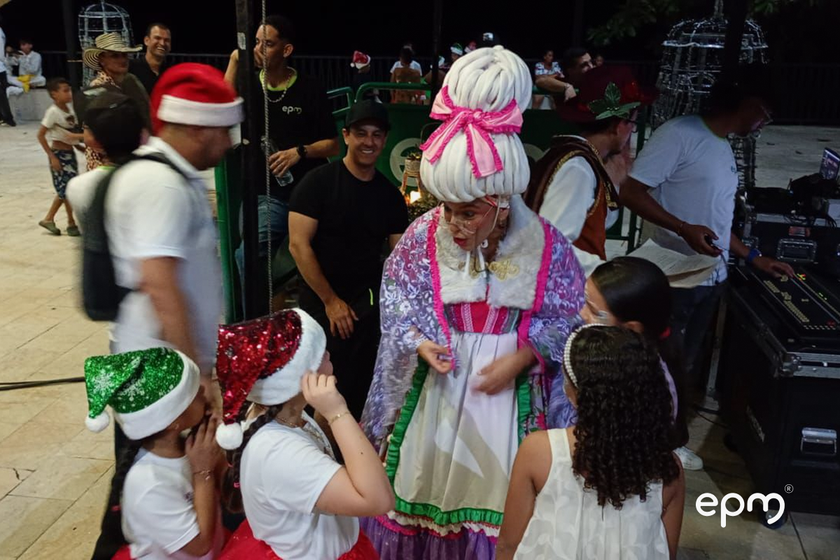 Niños con gorros de navidad comparten con actores de obra de teatro. Al fondo se observan personas dialogando