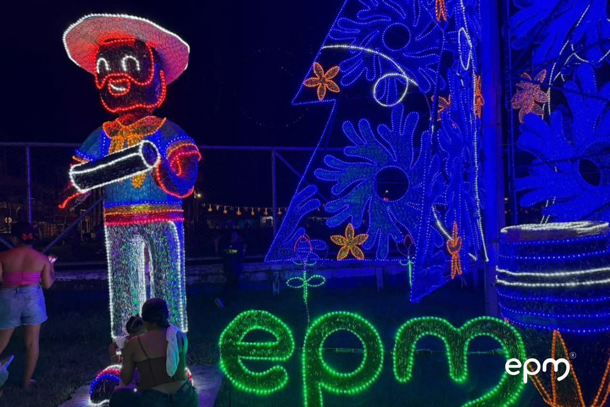 Figura navideña de hombre con sombrero acompañado de letrero en color verde de EPM. De fondo se observa alumbrado en color azul