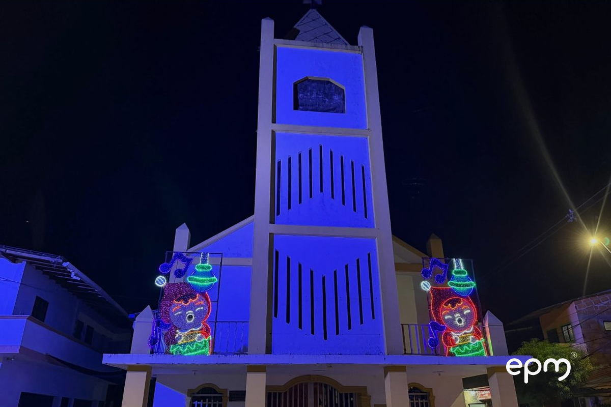 Fotografía de figura navideña de torre en color azul. De fondo se observan casas