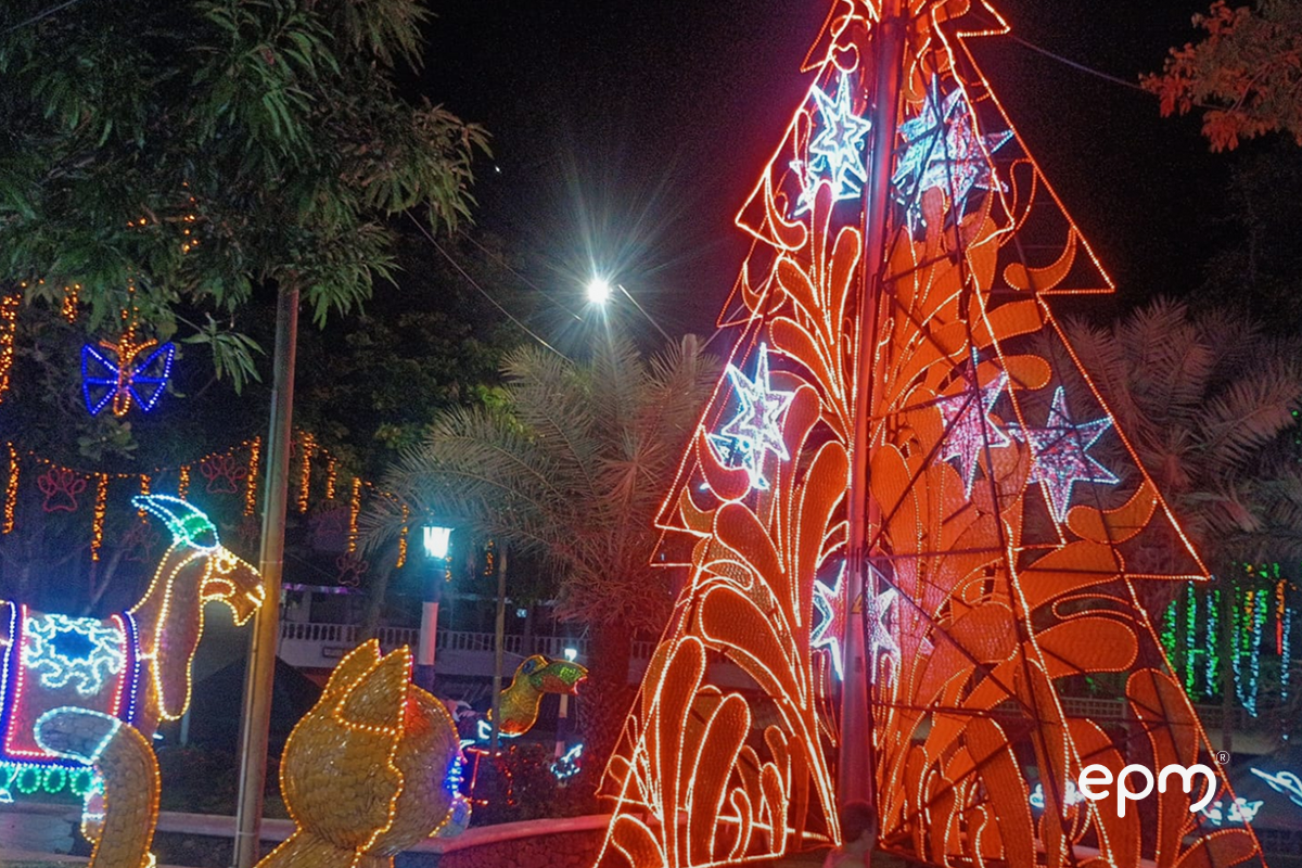 Figura de árbol navideño en color rojo y detalles claros, rodeado de árboles y figuras navideñas encendias