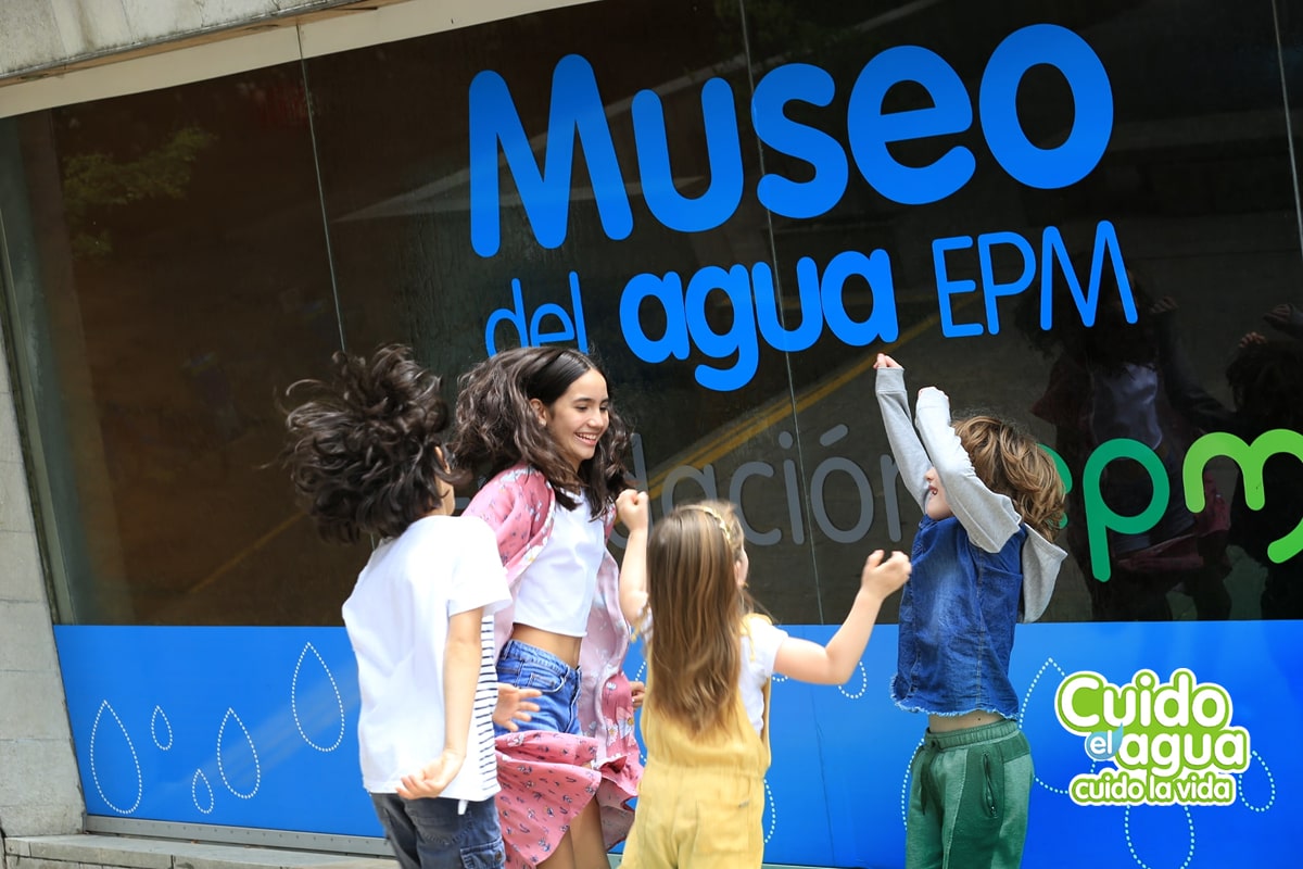 Fotografía de niños jugando frente al museo de agua epm, acompañadas de un sello que dice "Cuido el agua, cuido la vida"
