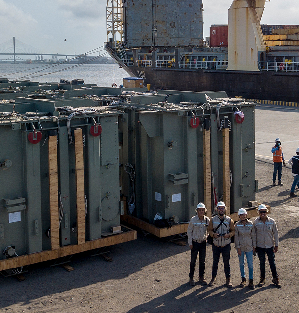 Grupo de transformadores industriales en un puerto, con un barco de fondo y varios trabajadores de EPM posando frente a los equipos.
