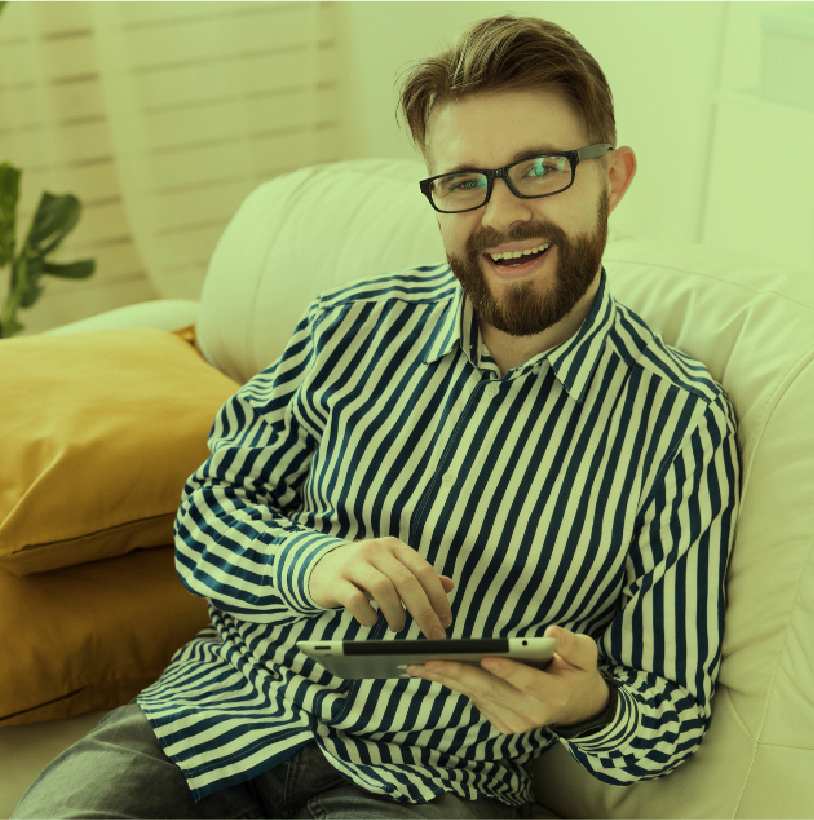 Hombre sonriente con gafas, sentado en un sofá, usando una tableta digital.