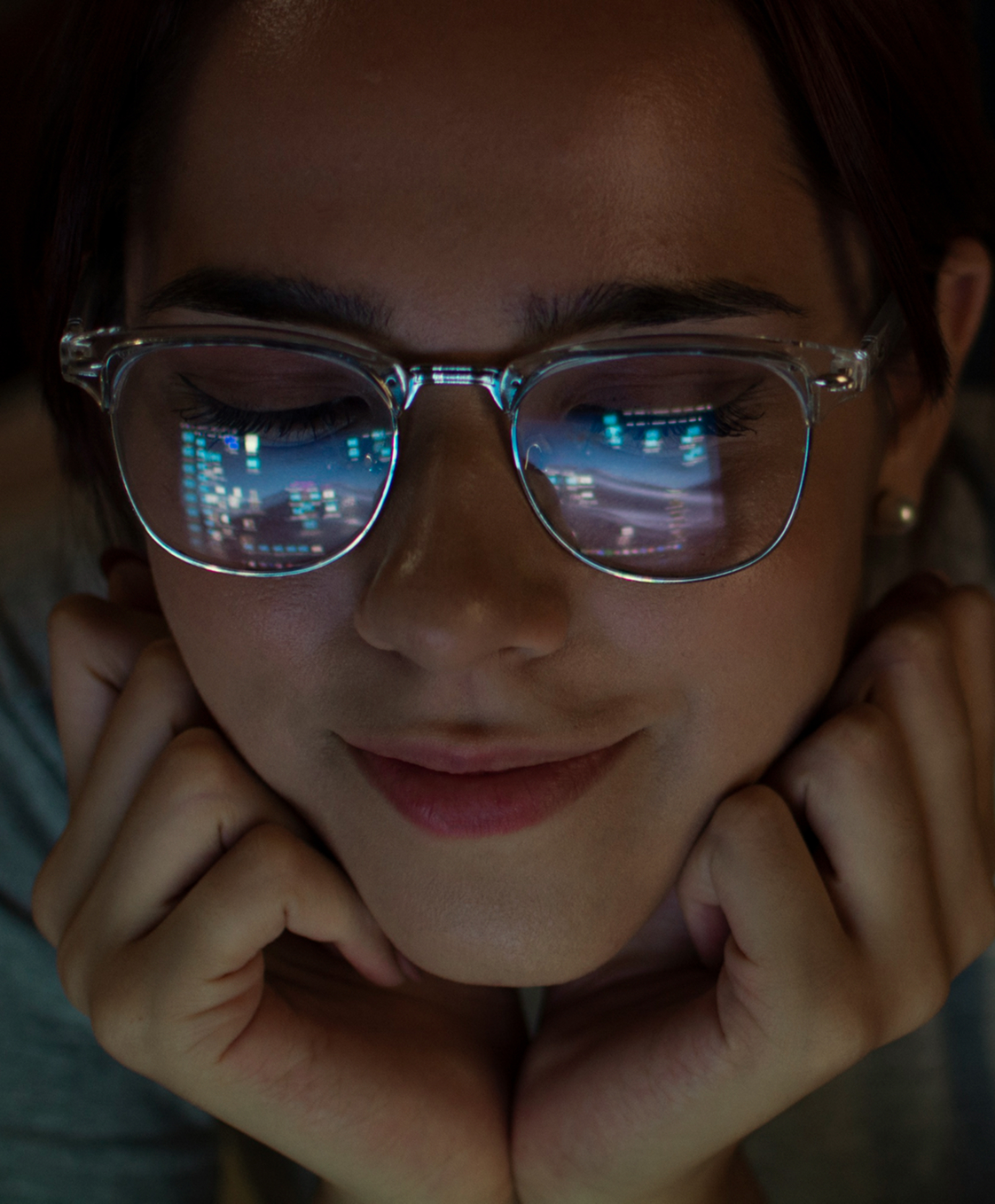 Mujer con gafas transparentes observa una pantalla; en el reflejo de sus lentes se distinguen gráficos y datos digitales iluminados.