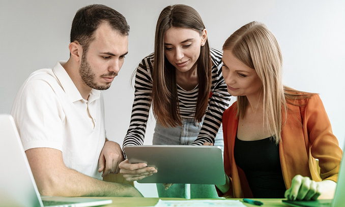 Tres personas observan juntas una tableta durante una reunión de trabajo en equipo.