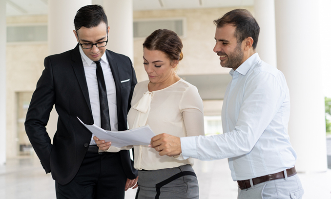Dos hombres y una mujer reunidos revisando unos documentos en un entorno corporativo