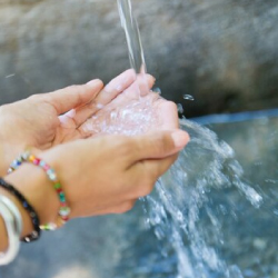 Manos de una persona recogiendo agua cristalina de un chorro natural, simbolizando el acceso al agua potable, el cuidado del recurso hídrico y el compromiso ambiental de EPM