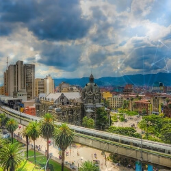 Vista panorámica del centro de Medellín con el edificio Rafael Uribe Uribe, el sistema Metro y espacios verdes, bajo un cielo parcialmente nublado, representando desarrollo urbano sostenible e innovación tecnológica impulsada por EPM