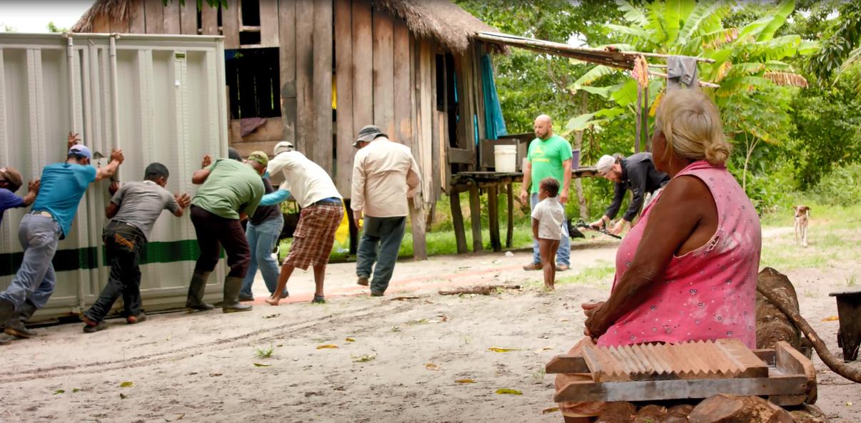 Comunidad rural colaborando en la instalación de infraestructura eléctrica de EPM, cerca de vivienda de madera en zona selvática