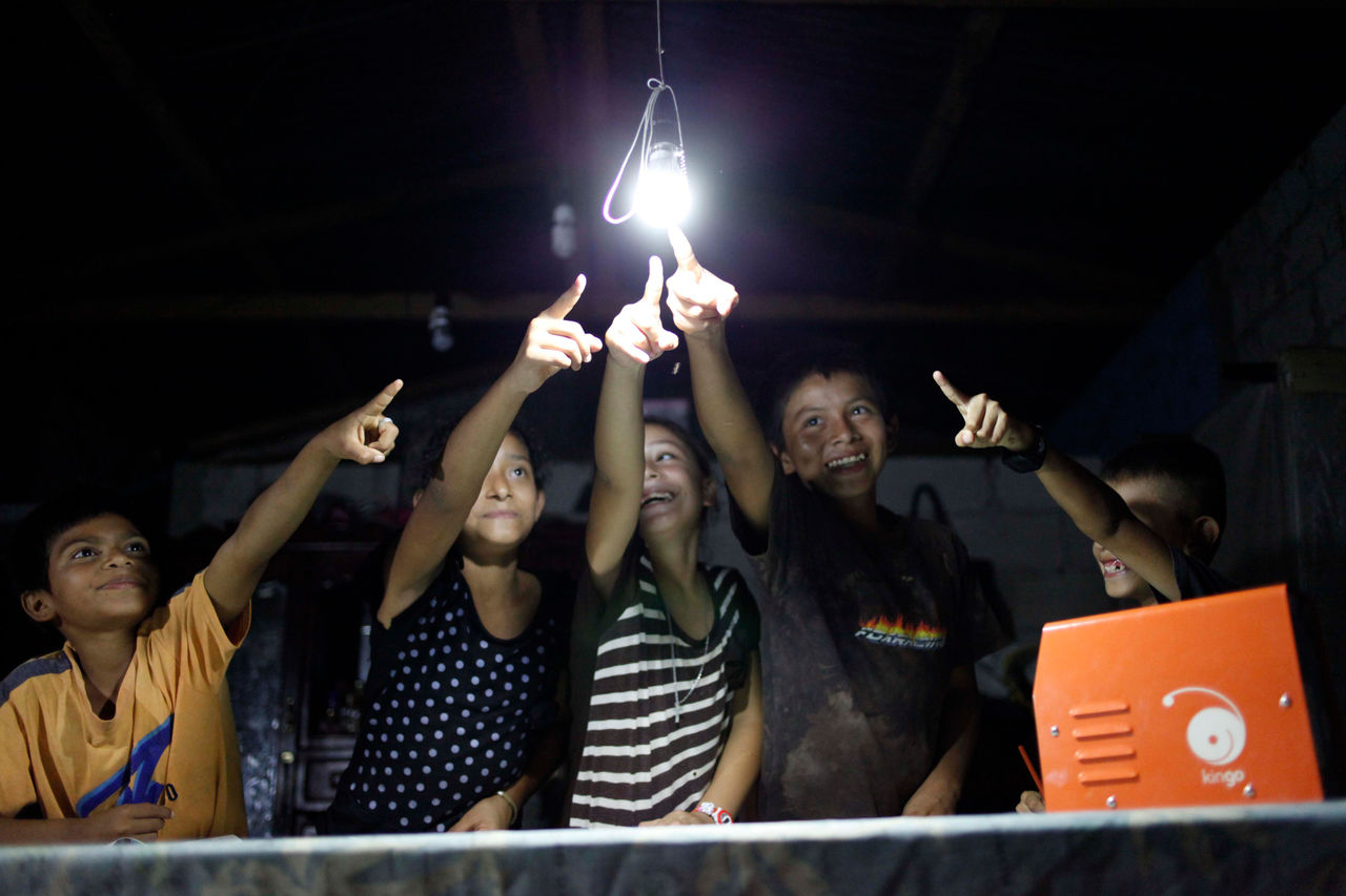Grupo de niños señalando un bombillo de luz eléctrica proporcionada por energía solar en comunidad rural