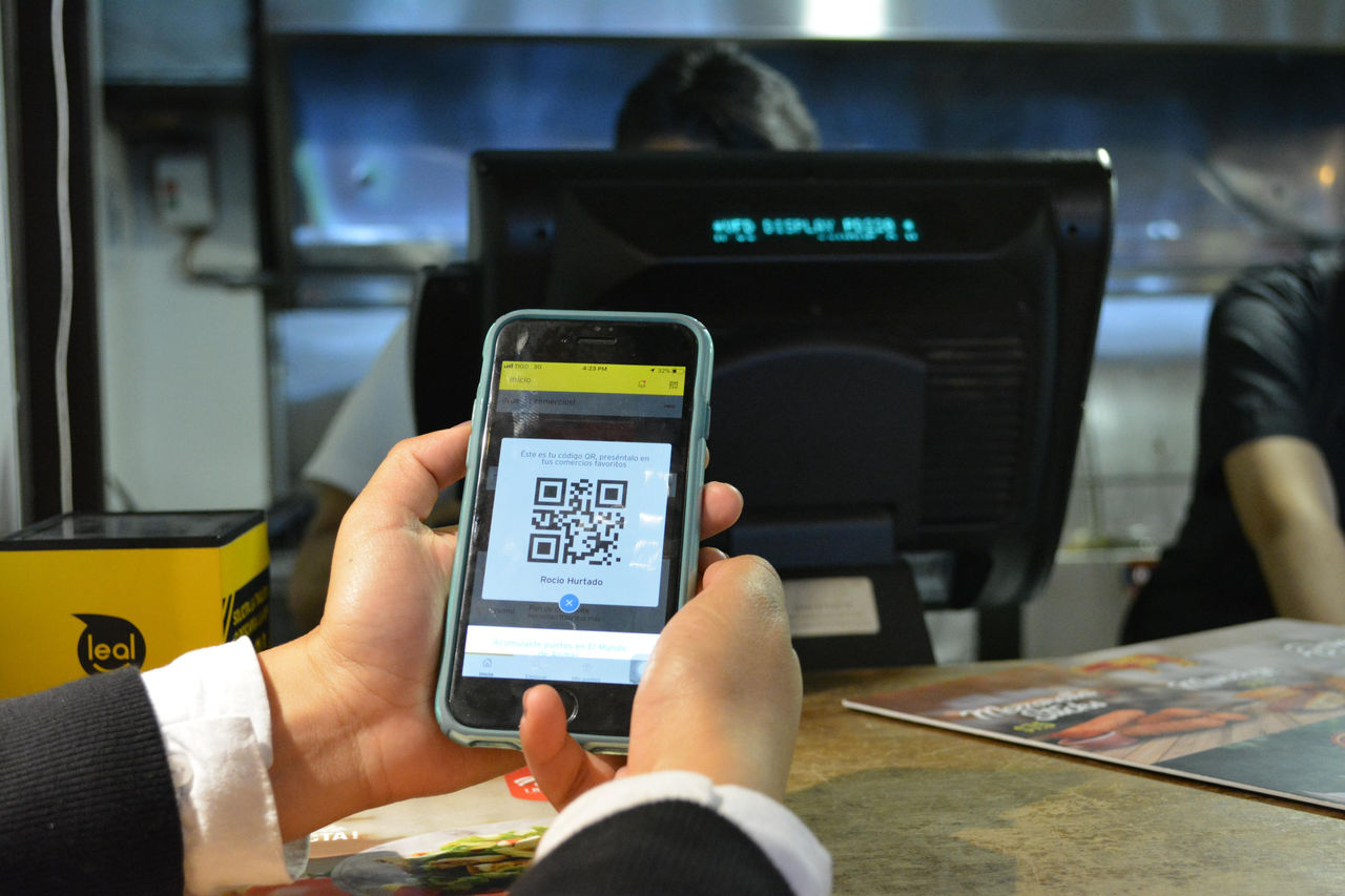 Persona escaneando código QR desde celular en comercio