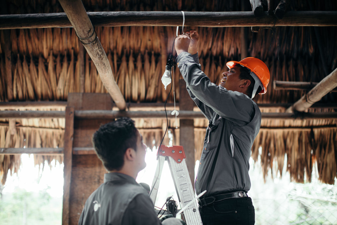 Técnicos de EPM instalan cableado eléctrico en vivienda rural con techo de palma
