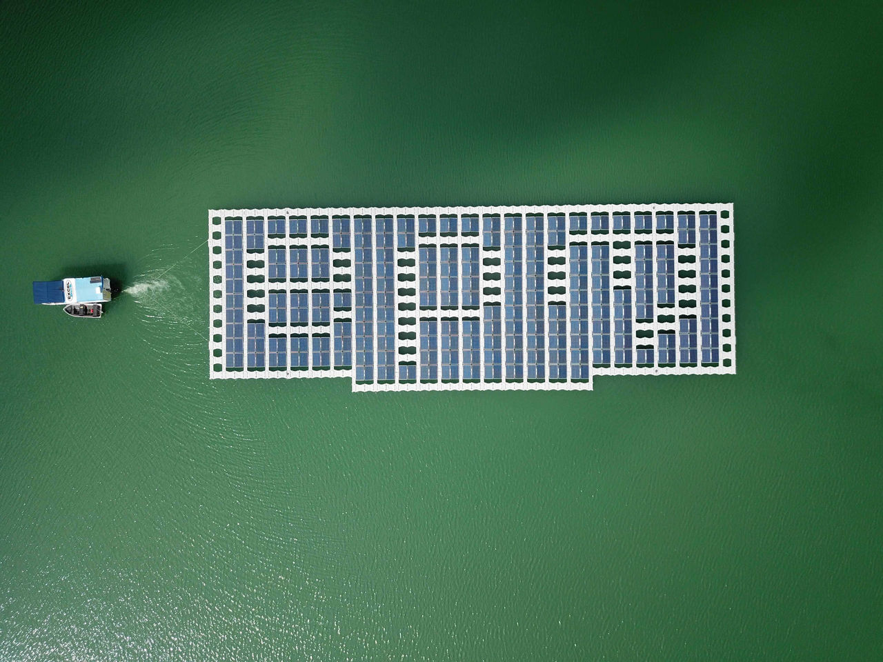 Plataforma solar flotante de EPM sobre embalse, vista aérea mostrando paneles solares generando energía limpia y renovable en cuerpo de agua verde