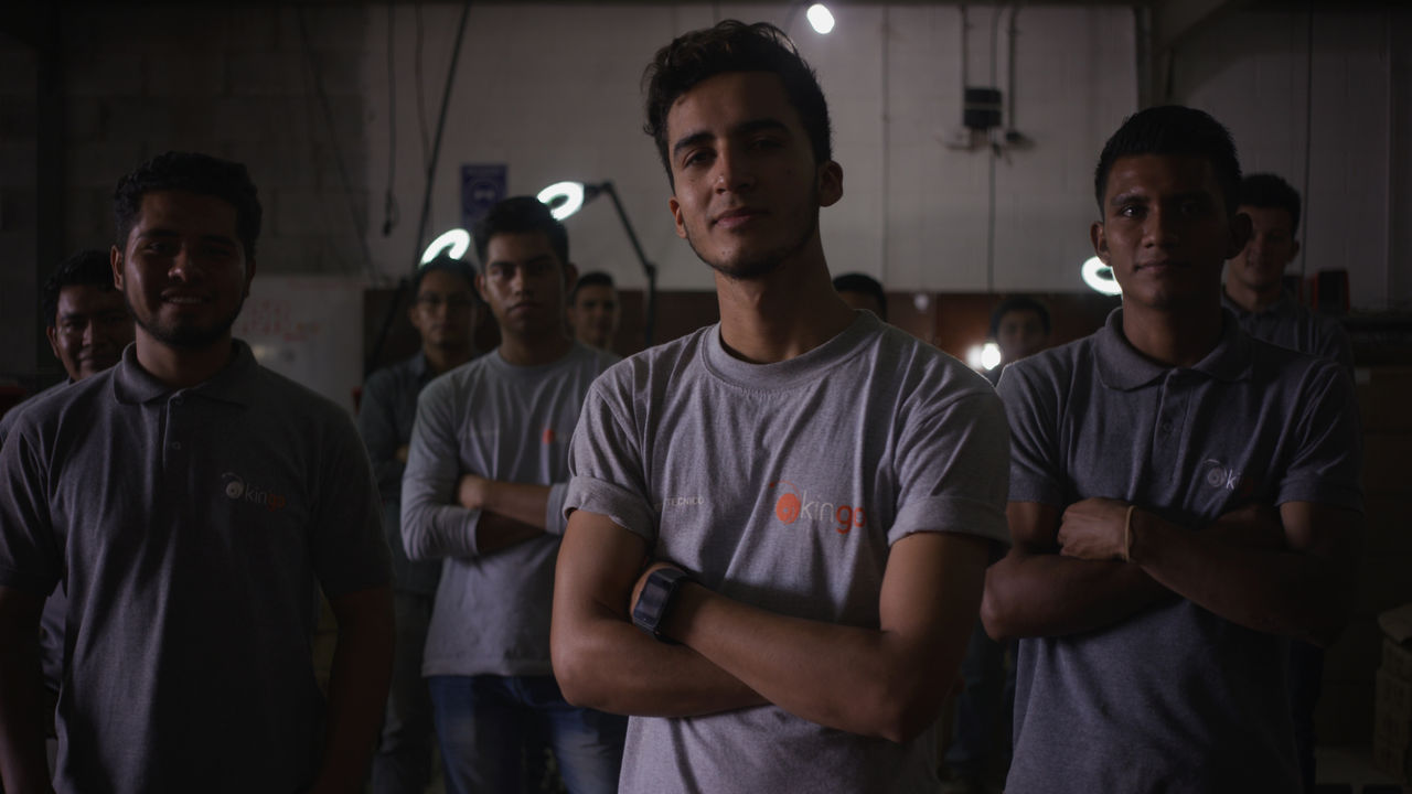 Grupo de jóvenes trabajadores con uniforme gris posando con confianza en espacio industrial iluminado