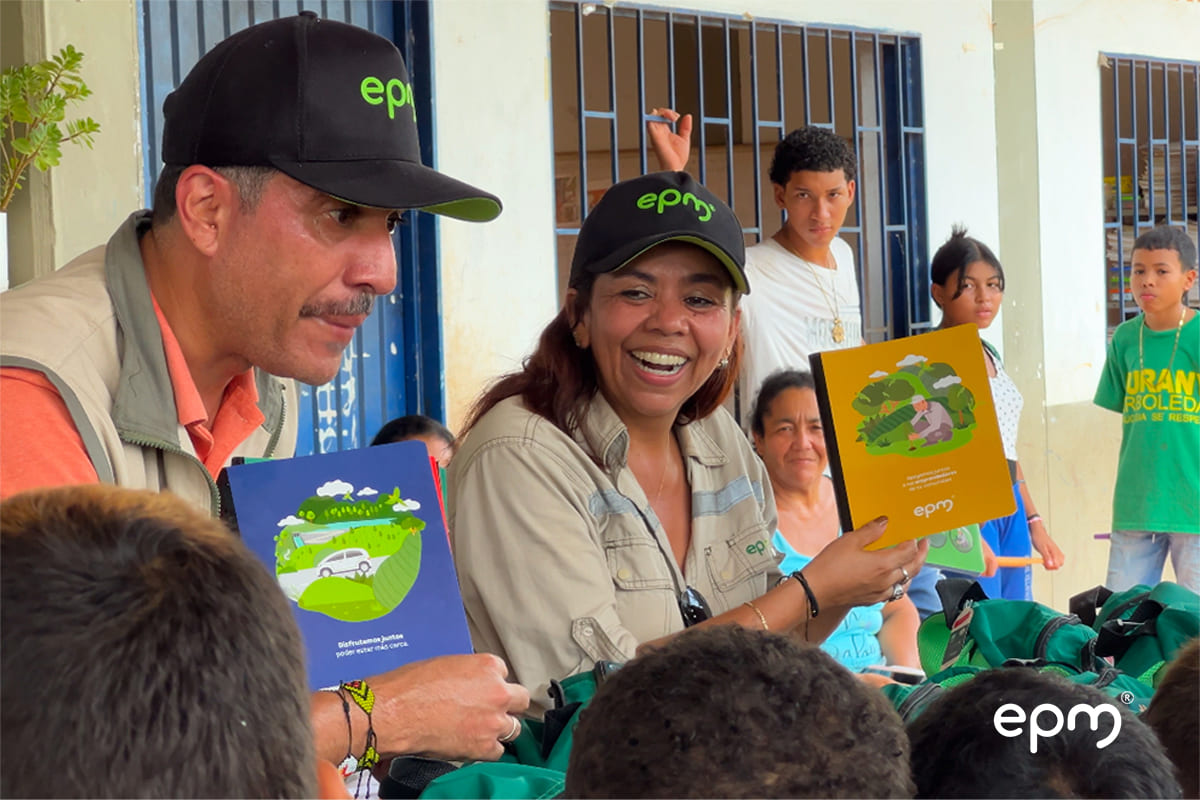 Funcionarios de EPM sonriendo dirigiéndose a un grupo de niños mientras entregan Kits escolares
