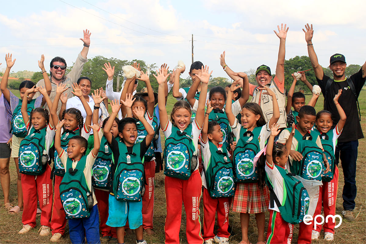 Grupo de niños sonrientes levantando sus manos en señal de alegría, mientras muestran sus nuevos kits escolares durante la entrega organizada por EPM.