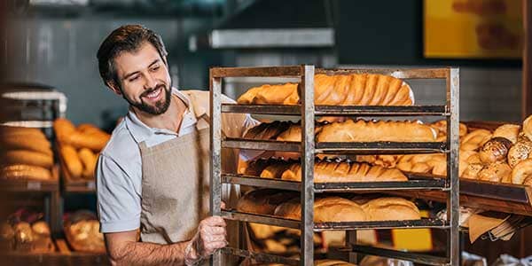 Panadero organizando bandejas llenas de pan fresco en una panadería.
