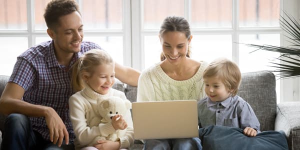 Familia feliz reunida en un sofá mirando una computadora portátil.