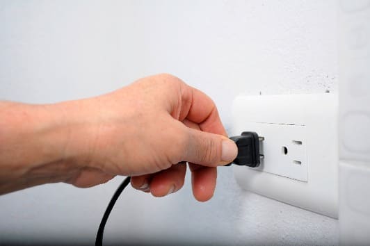 Imagen de mano sosteniendo un enchufe eléctrico mientras se inserta en una toma de corriente de pared. 