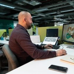 Si eres gente EPM, el acceso a está información tiene una imagen de un hombre sentado en un escritorio moderno, trabajando en un computador con doble pantalla.
