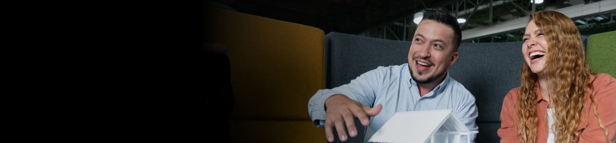 Hombre y mujer sonríen mientras observan una maqueta de casa en una oficina moderna