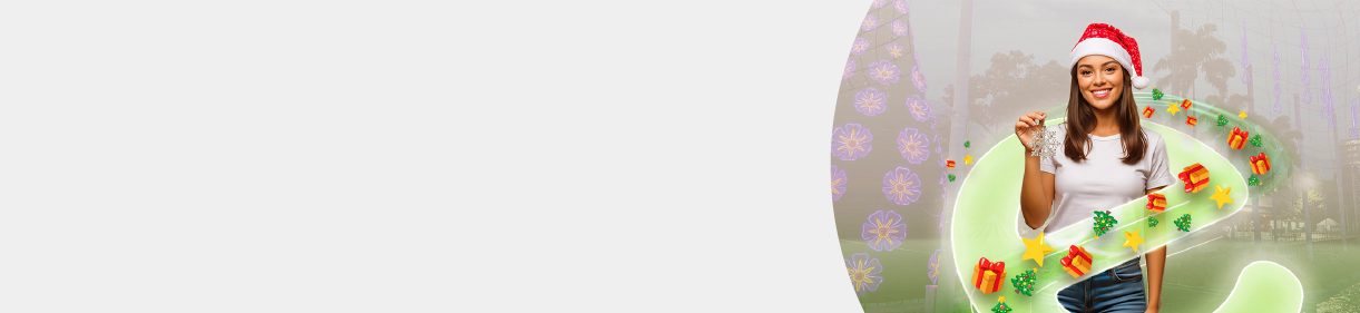 Mujer con gorro de Navidad sosteniendo un adorno frente a un árbol de luces