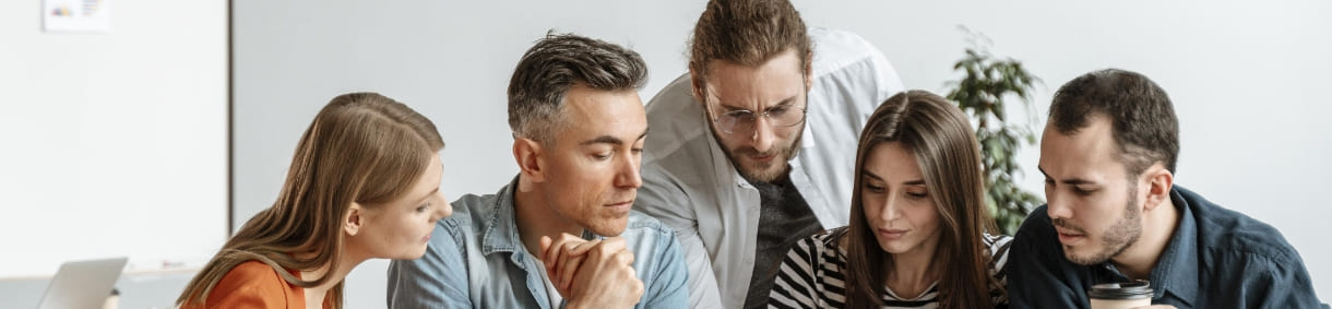 Equipo de trabajo de cinco personas reunidas, observando atentamente una pantalla o documentos en una sala de reuniones