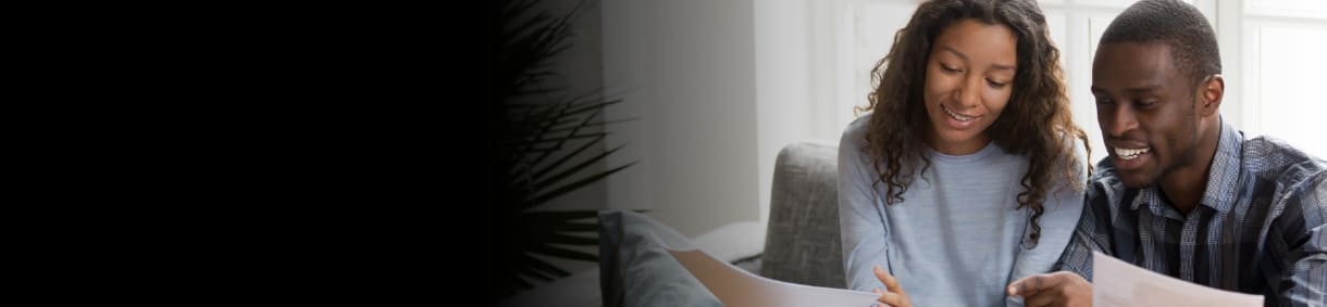 Pareja joven sonríe revisando documentos o facturas en la sala de su casa