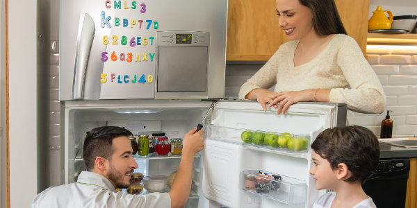 Hombre revisando la nevera abierta mientras una mujer y un niño observan con interés en una cocina moderna.