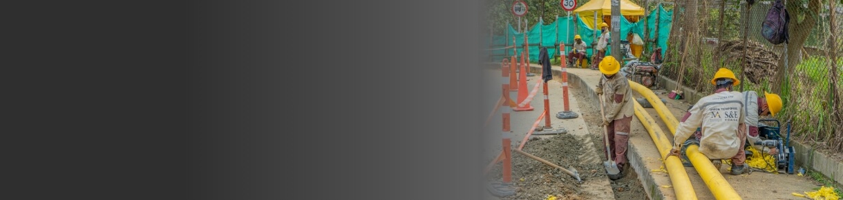 Trabajadores de EPM con cascos y uniformes instalan tuberías amarillas de gas natural en una zona rural, rodeados de señalización y vegetación