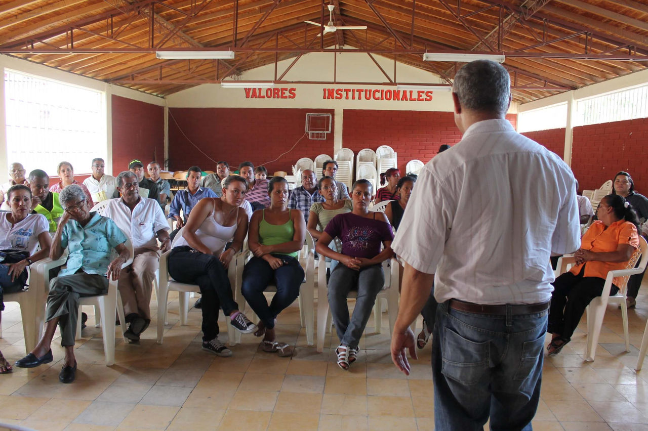 Fotografía de un hombre que se encuentra de espaldas a la cámara, dando una charla a padres de familias  
