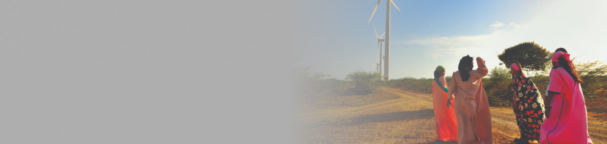 mujeres con vestimenta tradicional caminando cerca de aerogeneradores en un paisaje árido