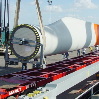 Transporte de una pala de aerogenerador sobre plataforma especial, levantada por grúa en zona industrial