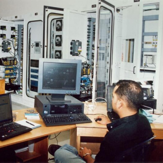 Hombre supervisa sistemas en sala de control con múltiples servidores y paneles electrónicos