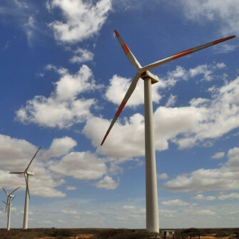Aerogenerador de gran altura en parque eólico sobre terreno árido, con cielo azul y nubes dispersas en segundo plano
