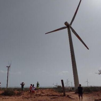 Imagen de personas observando un aerogenerador de gran tamaño en una zona desértica, bajo un cielo despejado.