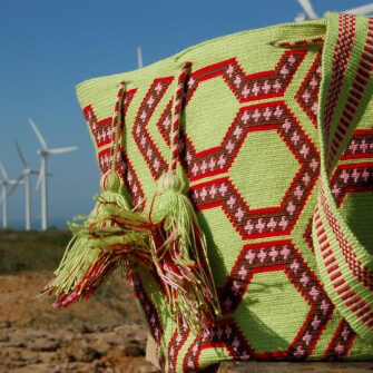 Imagen de mochila Wayuu tejida con diseño tradicional, con turbinas eólicas al fondo.